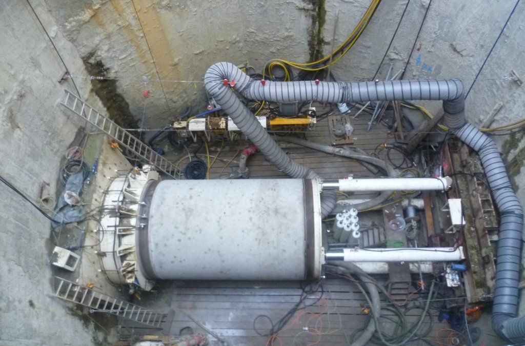 Tunnelbohrmaschine auf einer Baustelle. Graue Maschine, umgeben von Ausrüstung und Steinmauern.