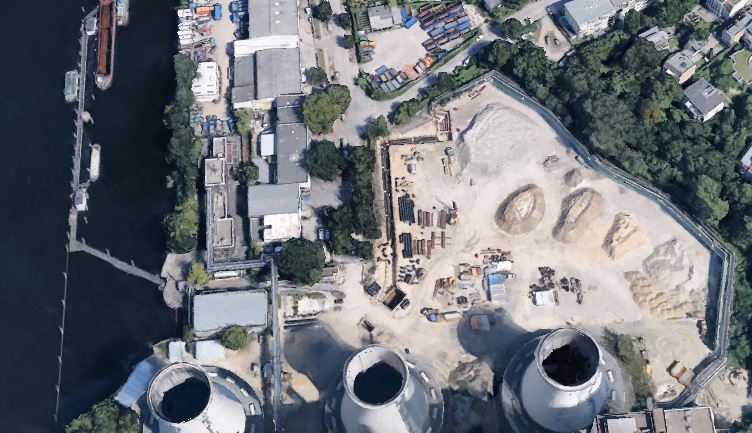 Luftaufnahme einer Baustelle neben einem Fluss mit Industriegebäuden und großen Kühltürmen aus Beton.