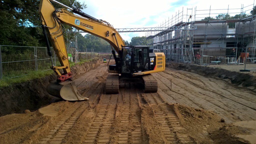 Gelber Bagger auf einem Feldweg an einer Baustelle.