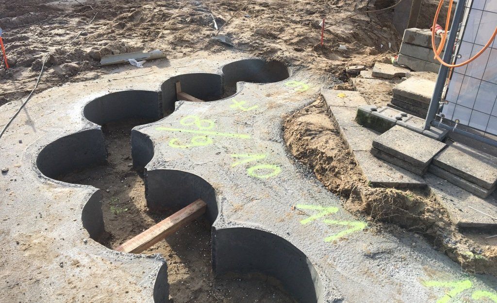 Baustelle: Betonplatte mit kreisförmigen Ausschnitten, Erde und einige Ziegelsteine.