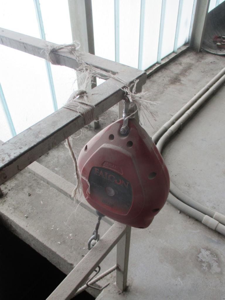 Ein rotes Werkzeug hängt an einem Seil an einem Metallträger in einem Innenraum mit Fenster.
