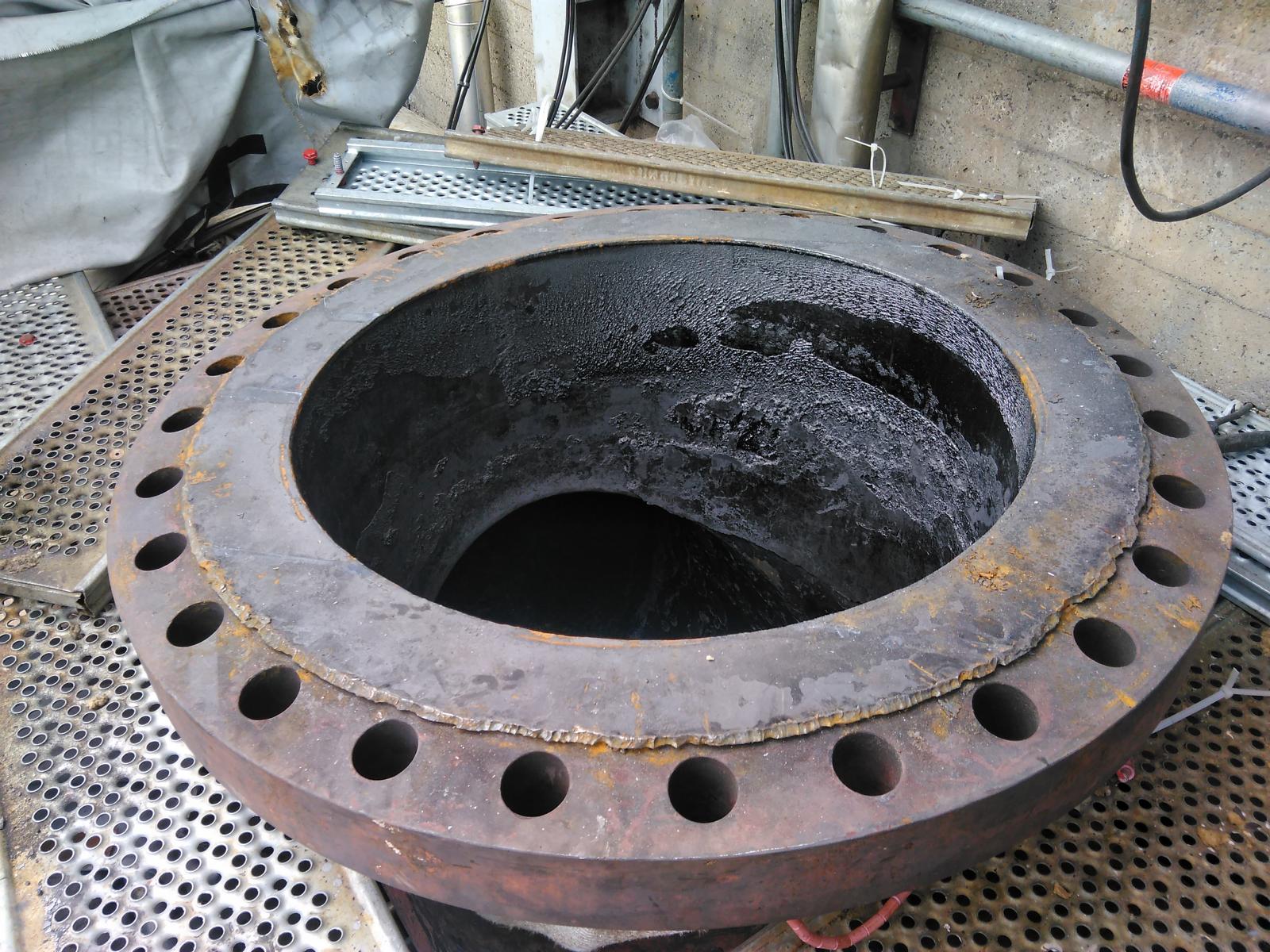 Großer, korrodierter Metallflansch mit Bolzenlöchern, im Inneren starke Lochfraßkorrosion und Ablagerungen.