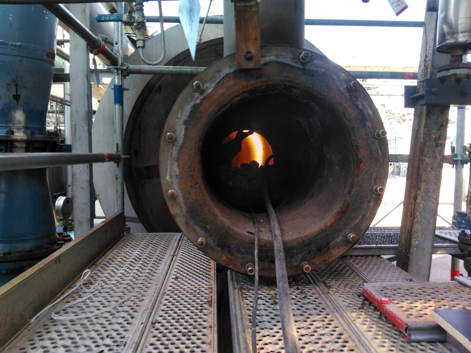 Das Innere eines Ofens, in dem durch eine große Metallöffnung Flammen sichtbar sind, industrielle Umgebung.
