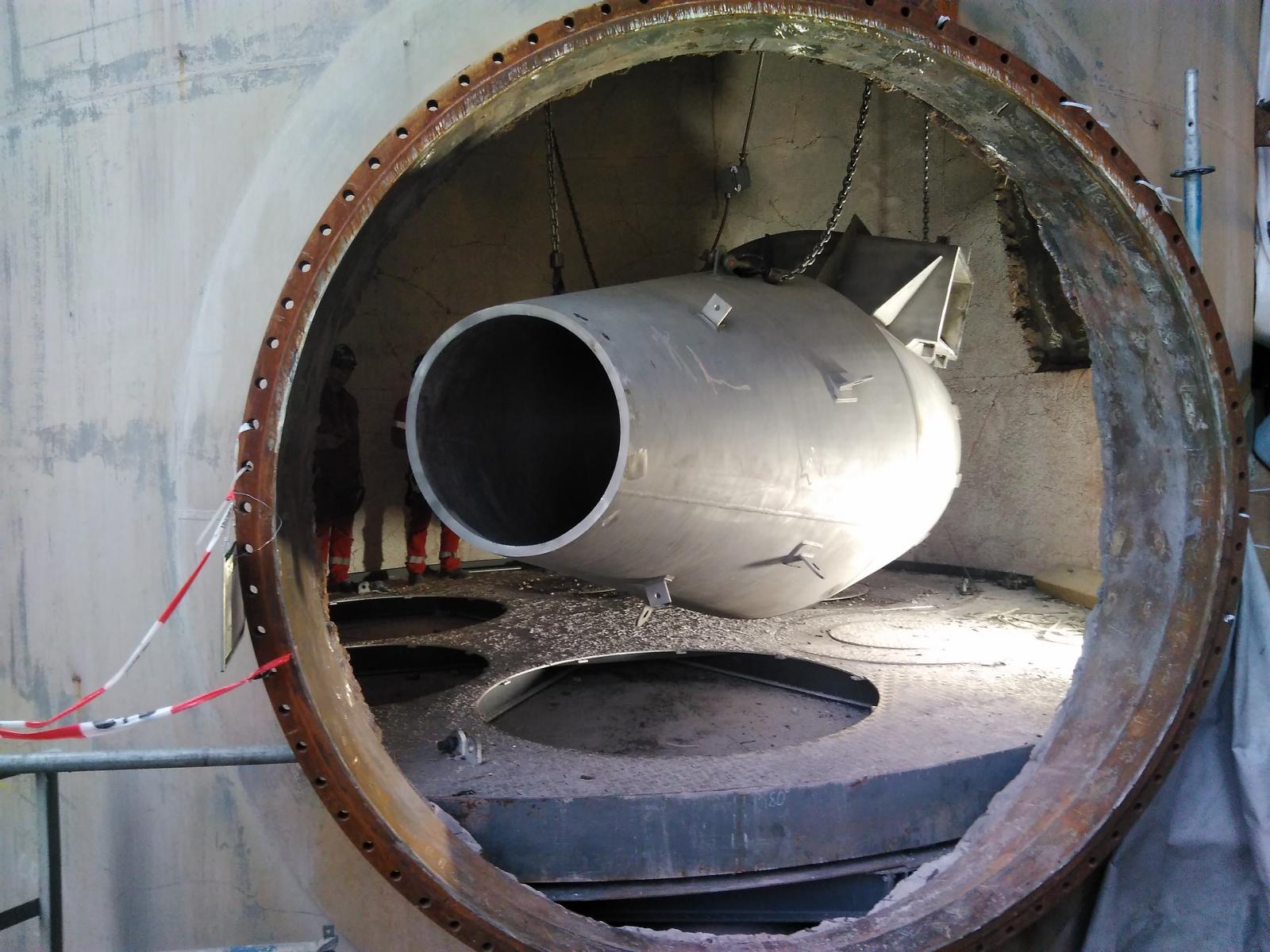 Große, zylindrische Metallkonstruktion mit einer runden Öffnung. Darin befindet sich ein abgerundetes, zylindrisches Objekt.