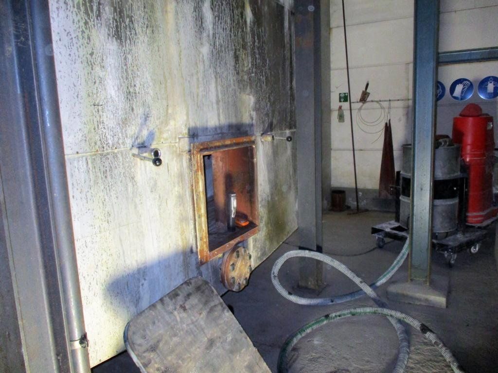 Schlauch, Werkzeug und Metallgerüst sind in einem schwach beleuchteten Industrieraum zu sehen.