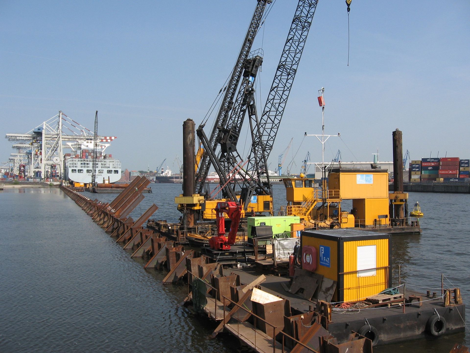 Ein Lastkahn mit Kran und Metallkonstruktion liegt in einem Hafen, vermutlich bei Ausbaggerungsarbeiten. 