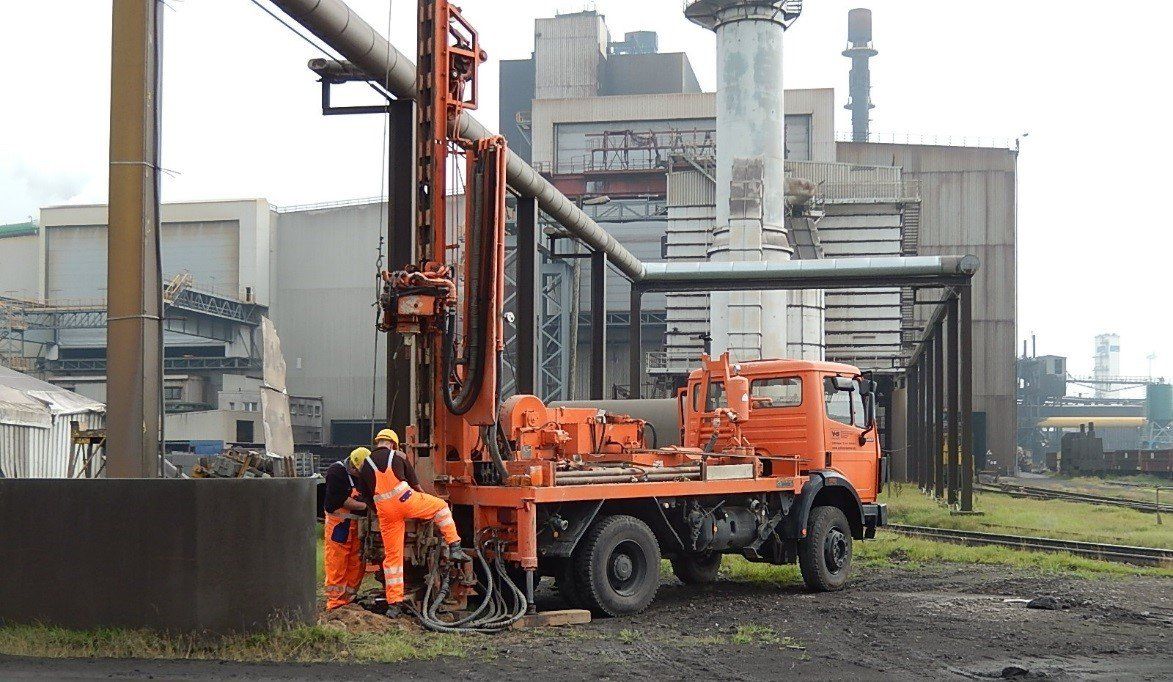 Orangefarbene Bohranlage mit Arbeitern in orangefarbenen Schutzanzügen in der Nähe einer Fabrik.