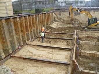 Baustelle mit Arbeitern, Bagger und Grabenverbau.