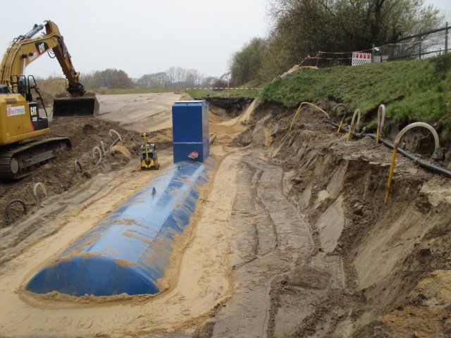 Ein blauer unterirdischer Lagertank wird von einem Bagger in einem Graben installiert. Baustelle.