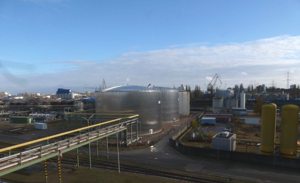 Große Industrietanks in einer Anlage mit Laufsteg, Rohrleitungen und Versorgungsanlagen vor blauem Himmel.