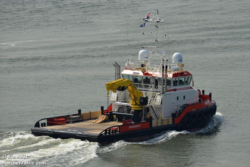 Ein orange-weißes Arbeitsboot fährt auf dem Wasser; an Deck befindet sich ein Kran und am Mast wehen Flaggen.