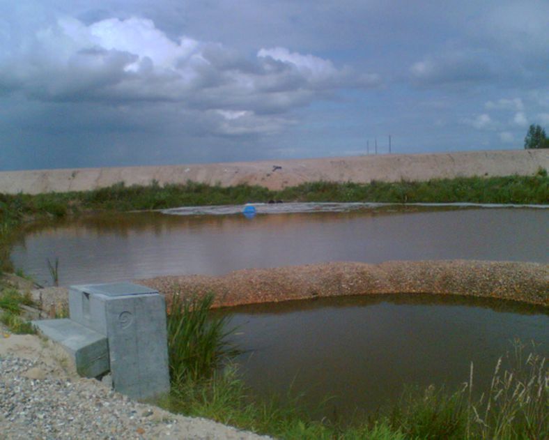 Ein trüber Teich mit einem Betonbauwerk im Vordergrund unter einem bewölkten Himmel.