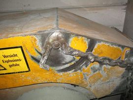 Gelbe und graue Metallvorrichtung mit Riegel und Kette, Warnschild sichtbar.