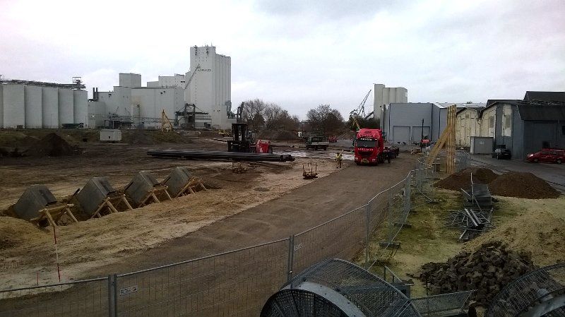 Baustelle mit LKW, Gebäuden und Maschinen an einem bewölkten Tag.