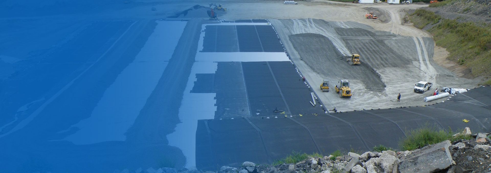 Baustelle mit schwerem Gerät und teilweise fertiggestellten Erdarbeiten. Blaue Markierung links.