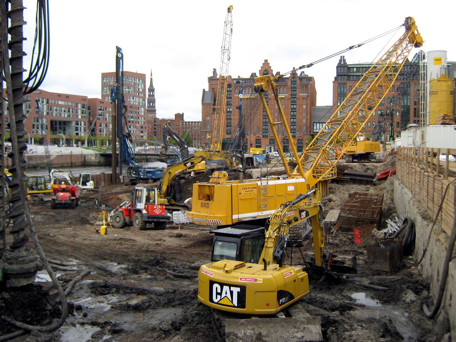 Baustelle mit gelben Kränen und Baumaschinen; im Hintergrund Gebäude.