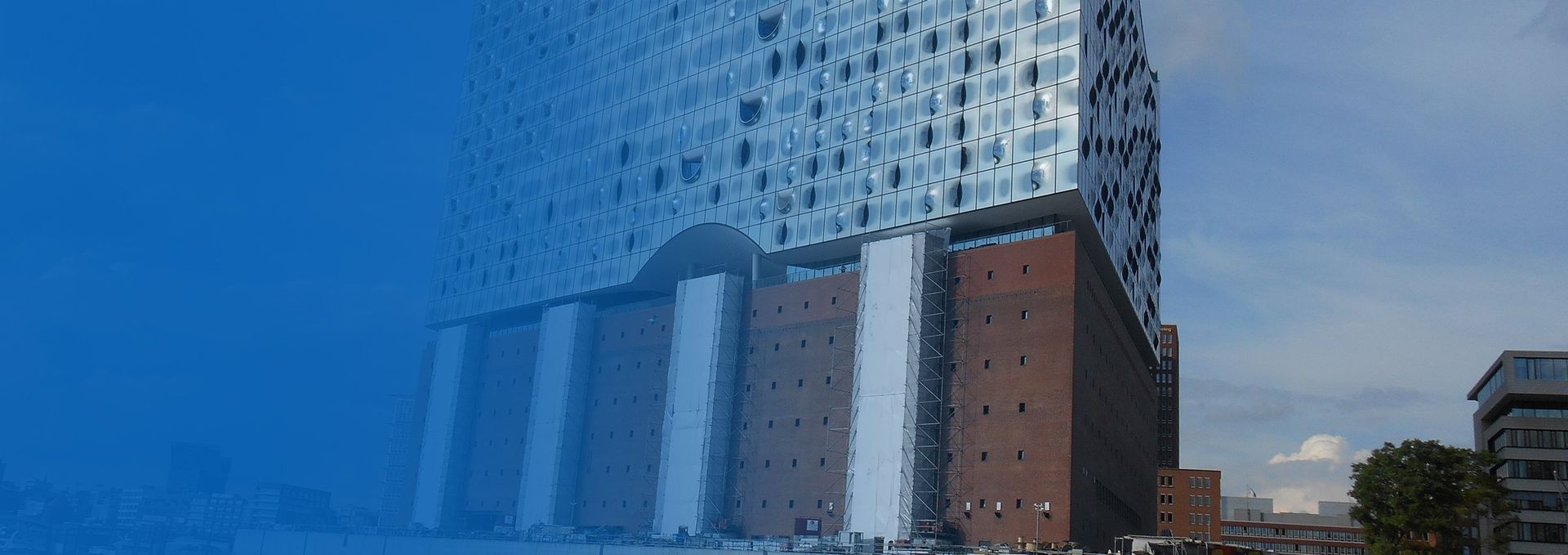 Elbphilharmonie, Hamburg, Deutschland, mit Glasfassade über einem Backsteingebäude, blauer Himmel.