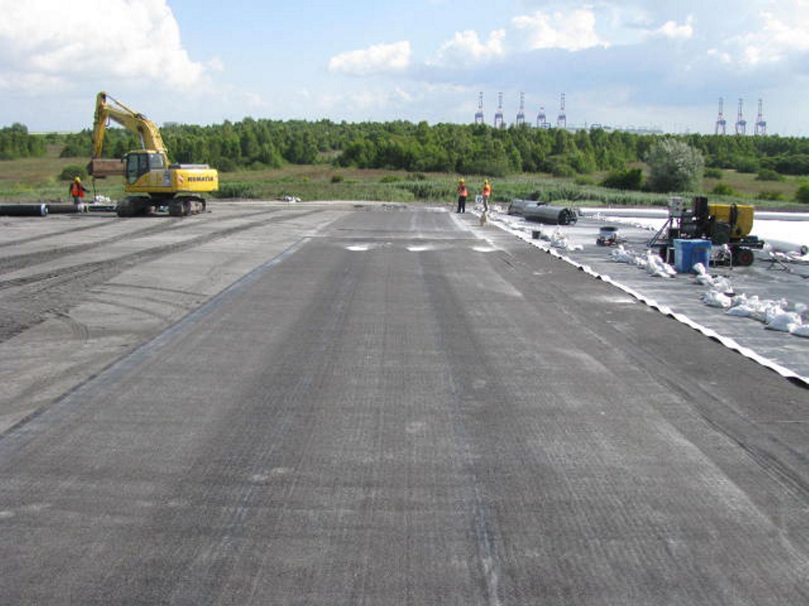 Baustelle mit Bagger und Arbeitern auf einer großen, ebenen Fläche.
