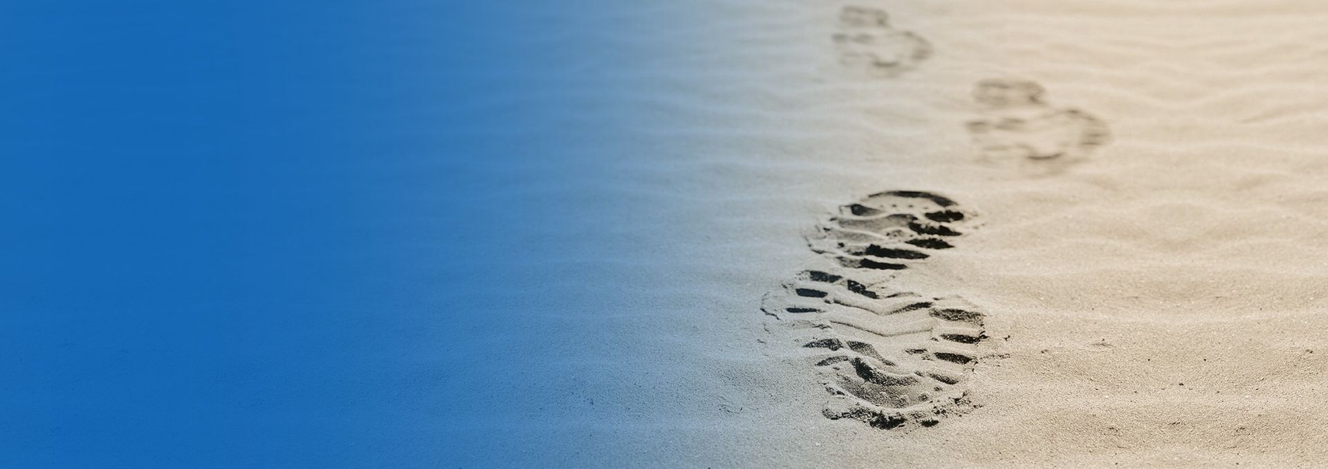 Fußabdrücke im Sand, die von Blau zu Beige verlaufen und einen Pfad andeuten.