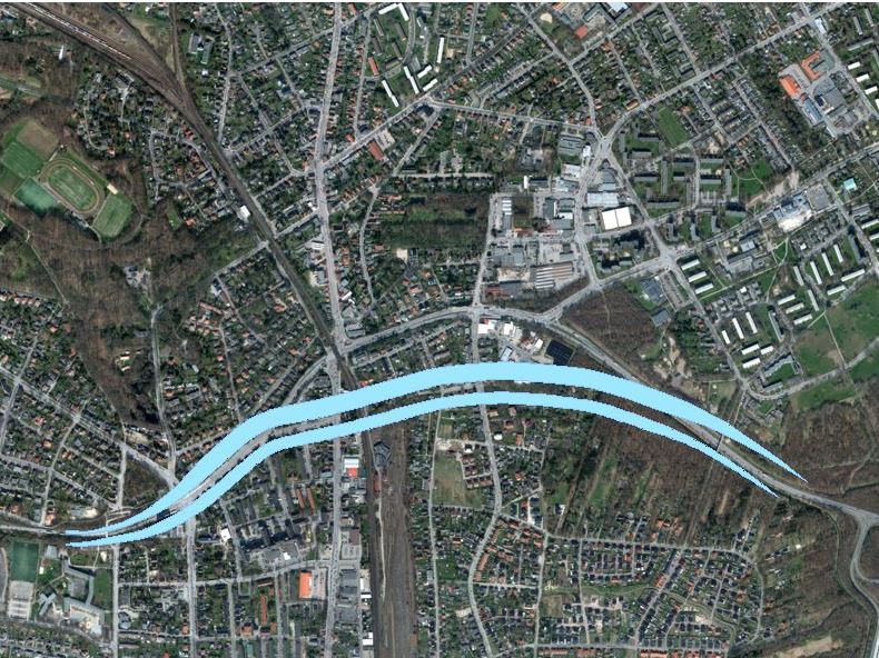 Luftaufnahme einer Stadt mit einer blau hervorgehobenen, geschwungenen Straße, die durch Wohn- und Gewerbegebiete führt.