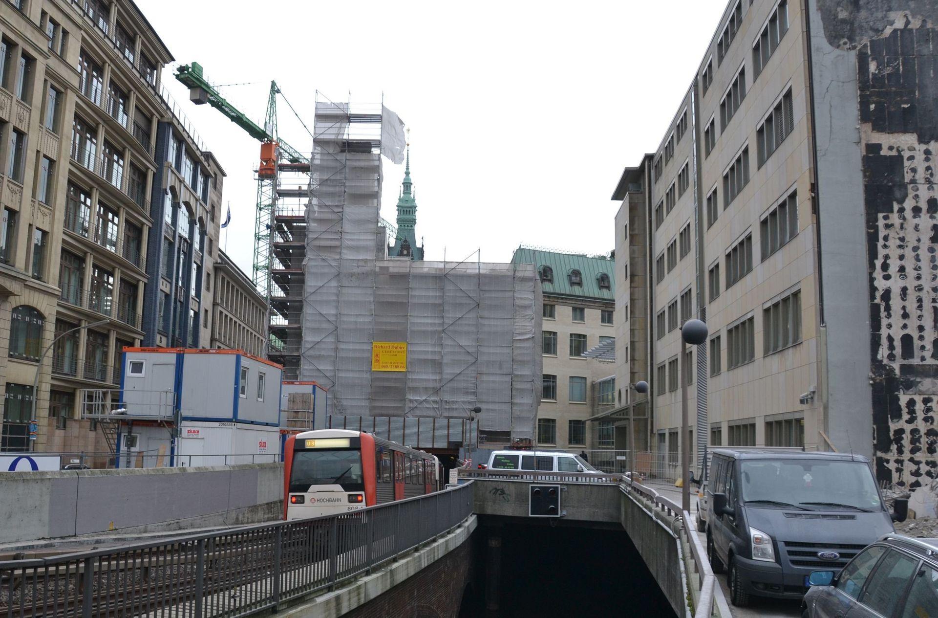 Straßenszene mit Baustelle, Gebäuden, Autos und einer Straßenbahn.