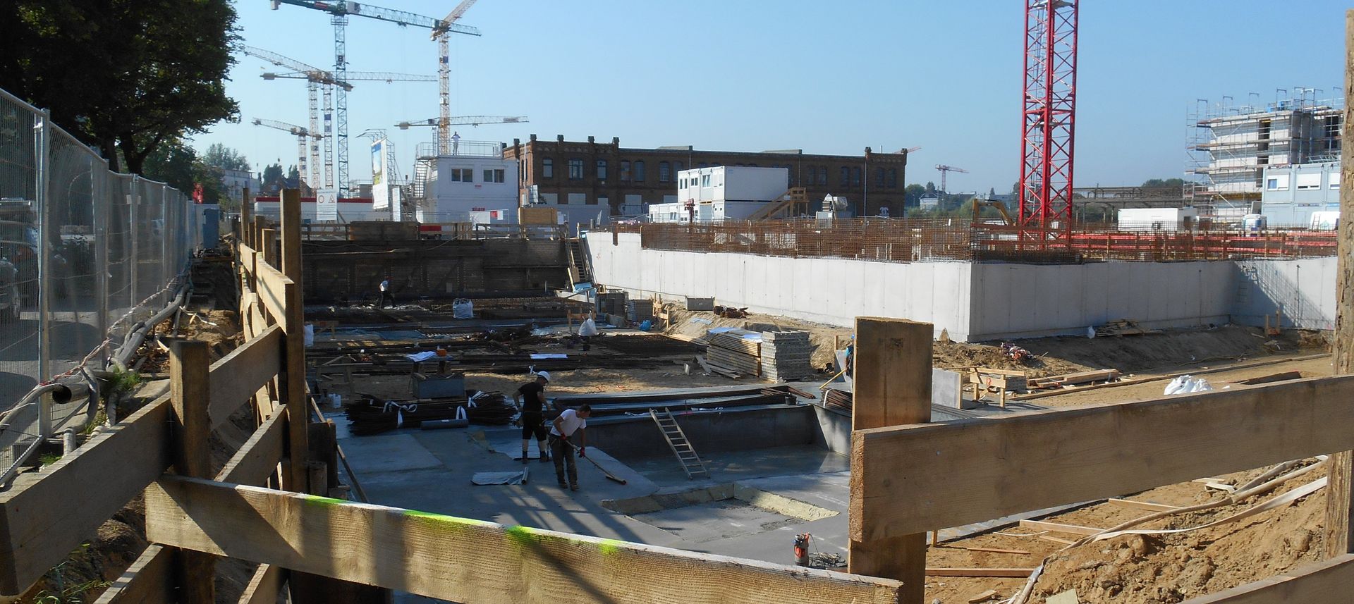 Baustelle mit Kränen, Betonkonstruktionen und Arbeitern an einem sonnigen Tag.