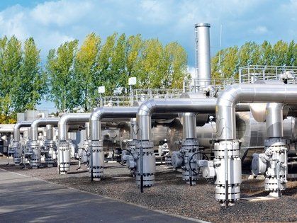 Silberne Industrierohre und -anlagen, Außenaufnahme, grüne Bäume im Hintergrund.
