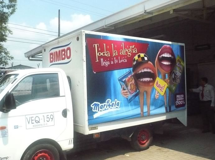 Camión de reparto Bimbo con un colorido anuncio publicitario en una valla que muestra personajes
