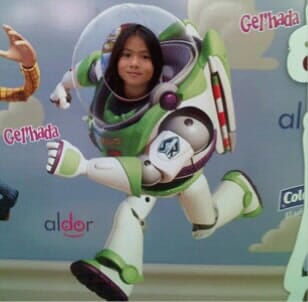 Un niño posando con un disfraz de Buzz Lightyear, con una silueta de cara sonriente y logotipos de patrocinadores al fondo.