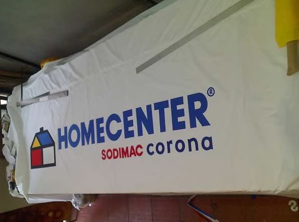 Letrero blanco de Homecenter SODIMAC Corona colgado en el interior, con texto del logotipo en azul y rojo.