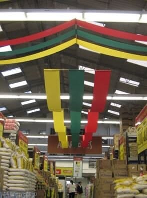 Pasillo de supermercado decorado con banderines rojos, verdes y amarillos colgando sobre sacos y estantes apilados.