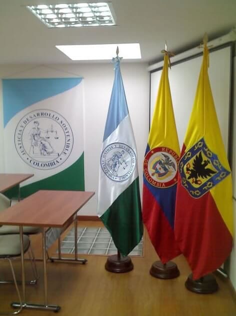 Sala con tres banderas de pie junto a un atril y una pancarta en la pared en un espacio para reuniones formales.