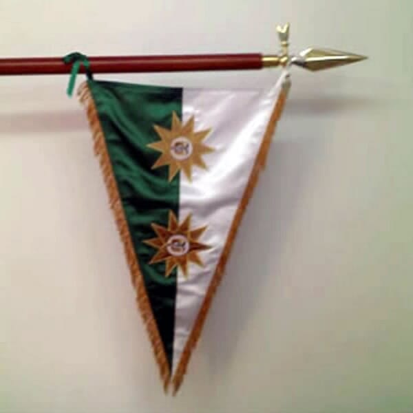 Banderín triangular blanco y verde con dos emblemas dorados colgando de una lanza en una pared.