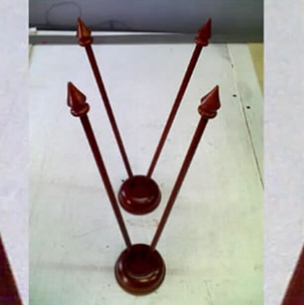Dos soportes decorativos de metal color burdeos con puntas en la parte superior sobre una superficie blanca.