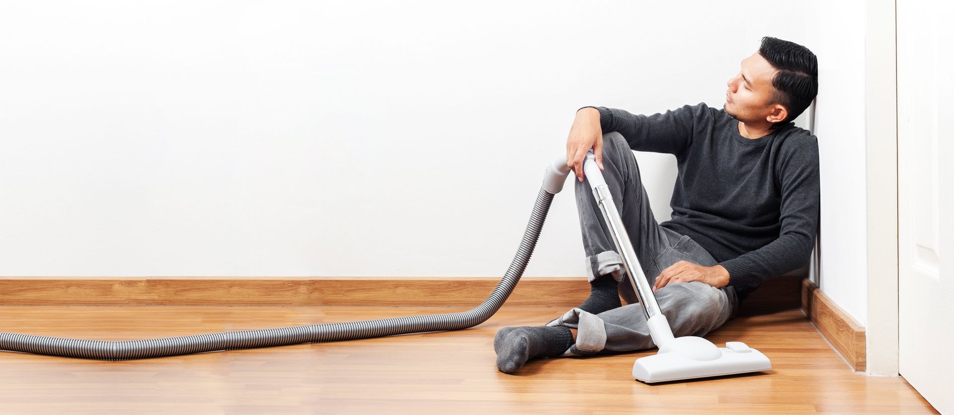 A man is sitting on the floor using a vacuum cleaner.