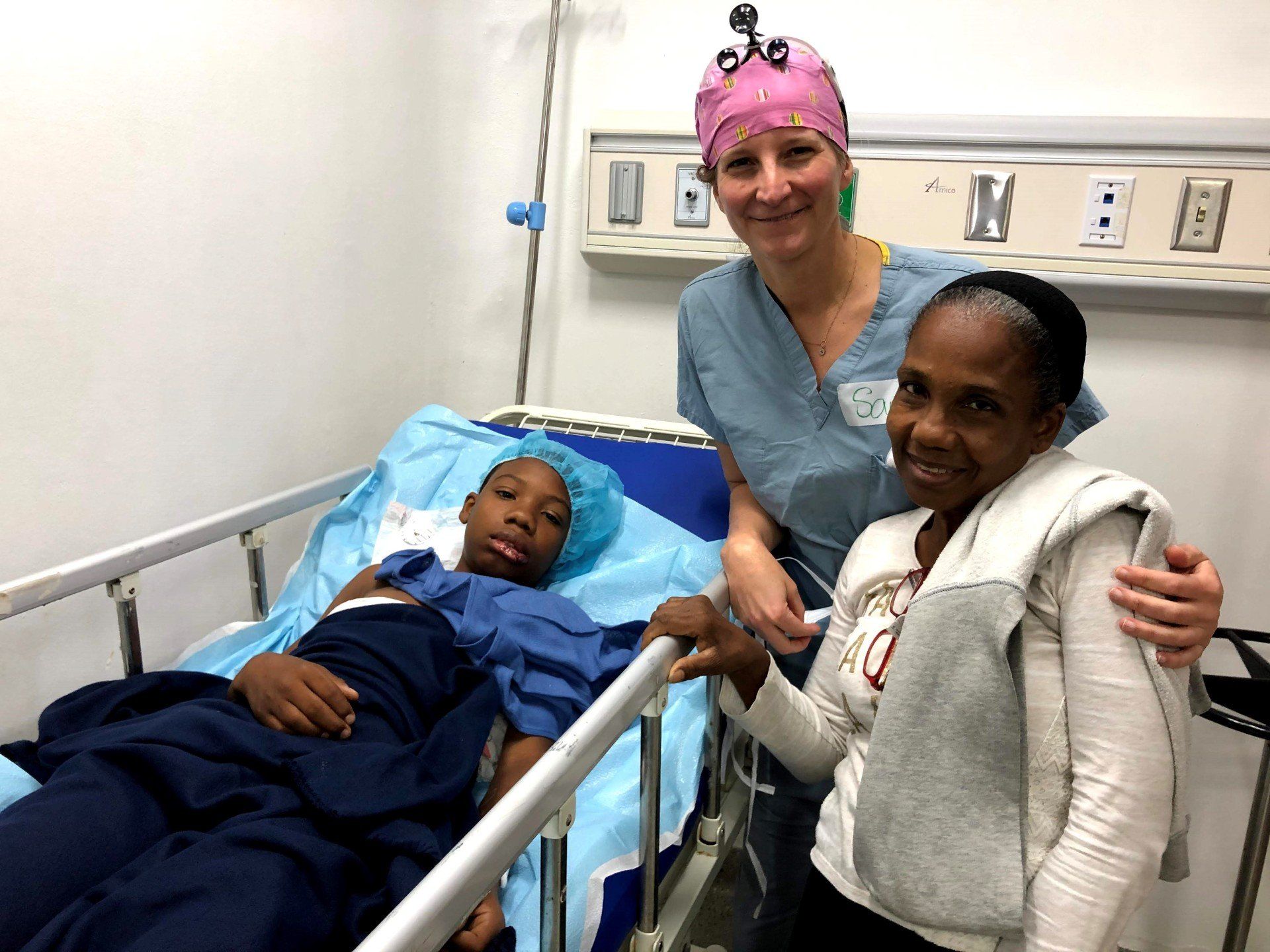 Two women are standing next to a child in a hospital bed.