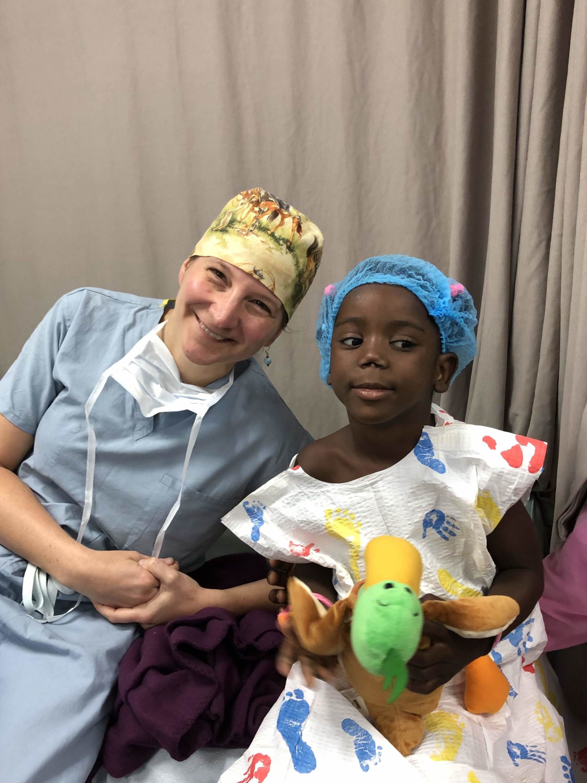 A nurse is sitting next to a little girl who is holding a stuffed animal