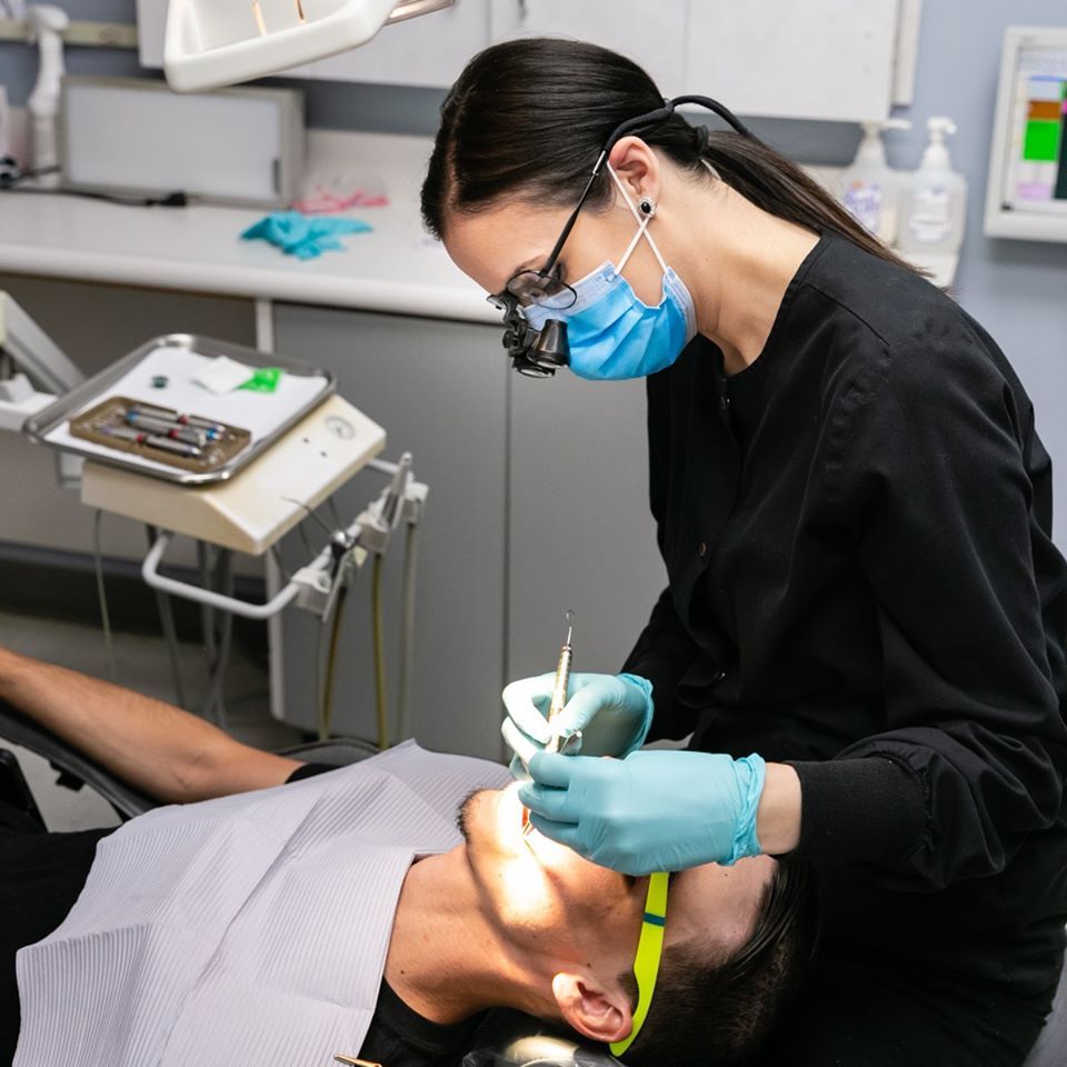 A female dentist is examining a man 's teeth in a dental office.