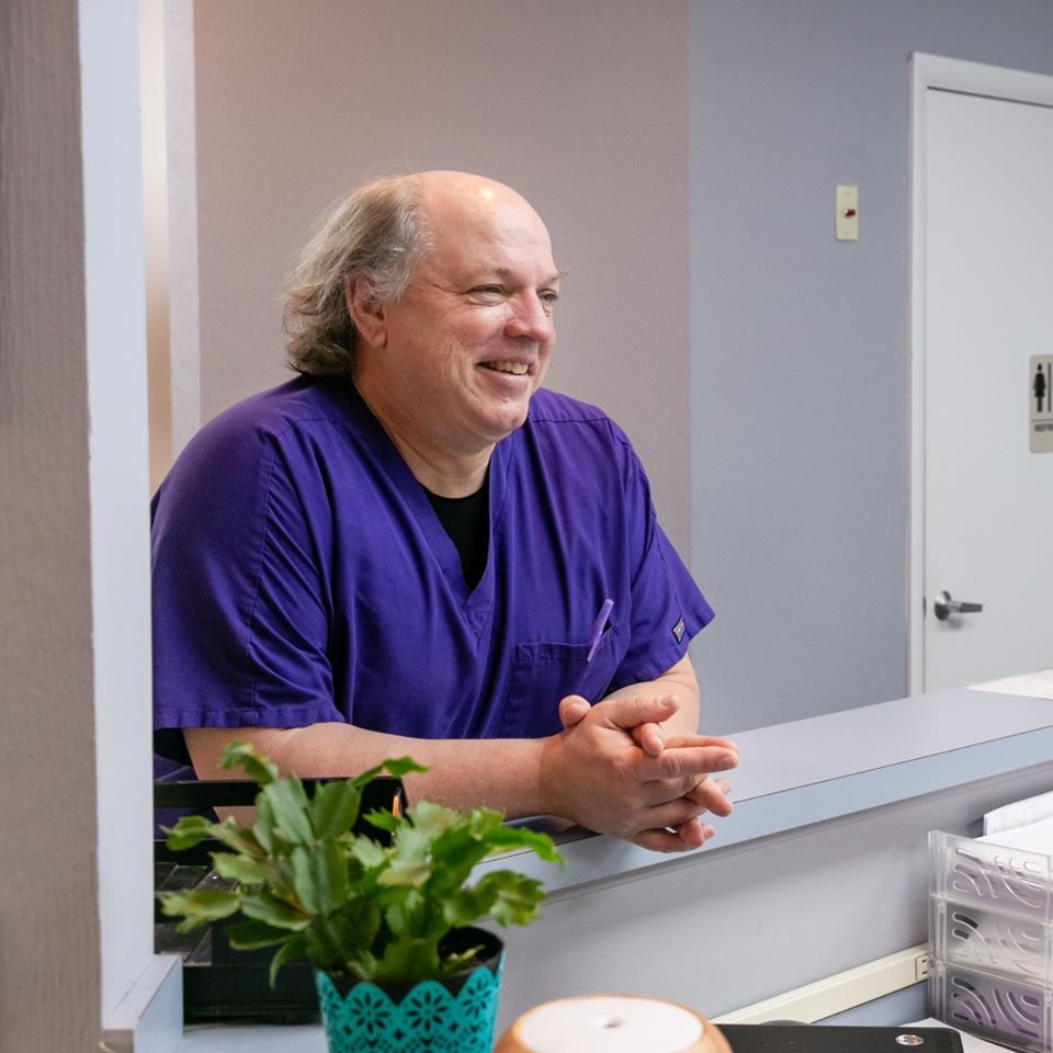 A man in a purple scrub is sitting at a counter and smiling