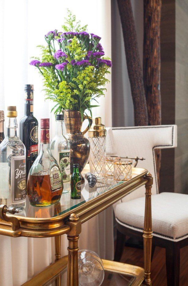 A bar cart with bottles of liquor and a vase of flowers on it.