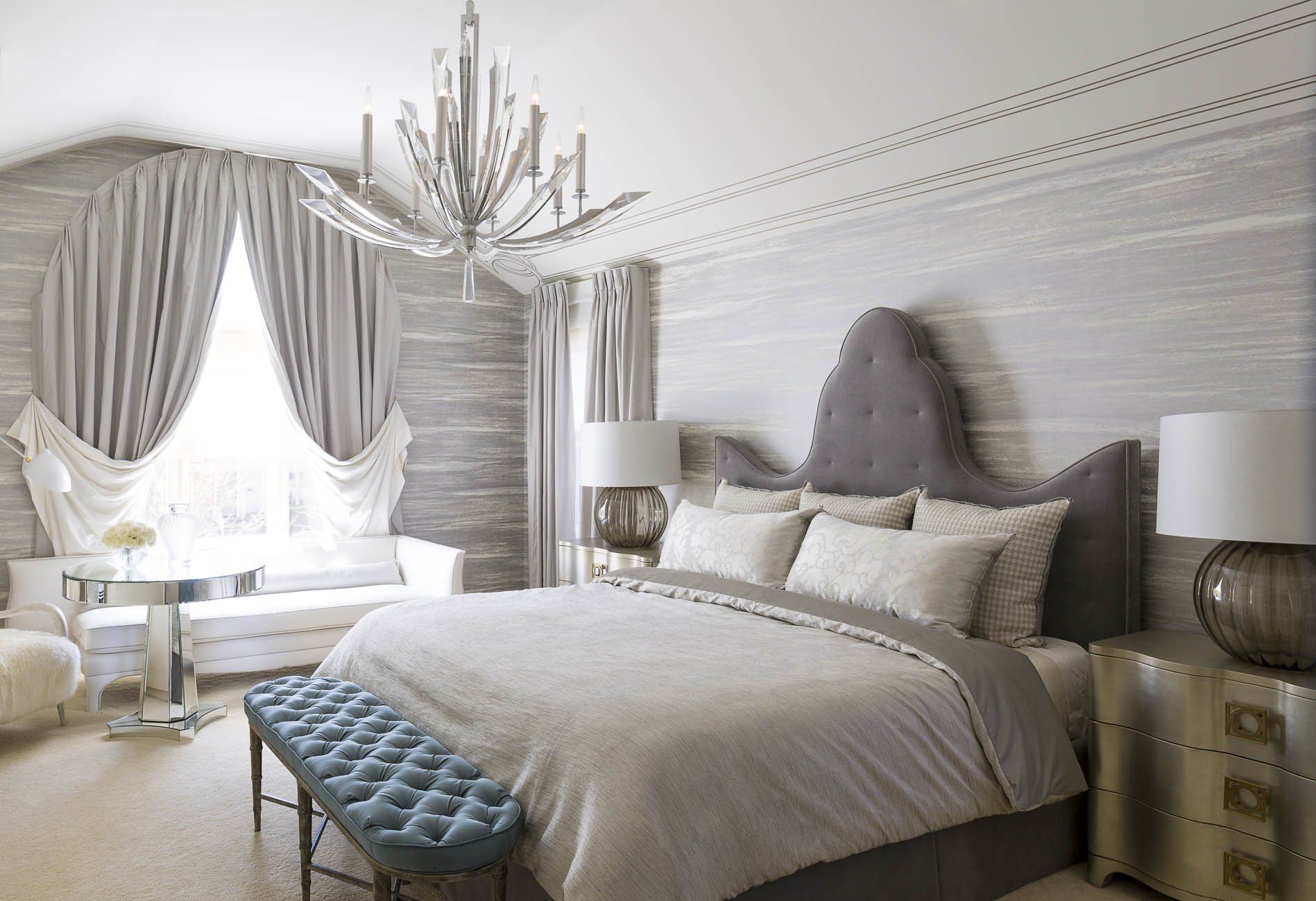 A bedroom with a large bed , a bench , lamps and a chandelier.