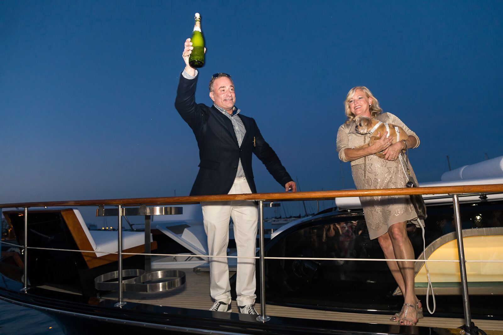 A man is holding a bottle of champagne while standing next to a woman on a boat.