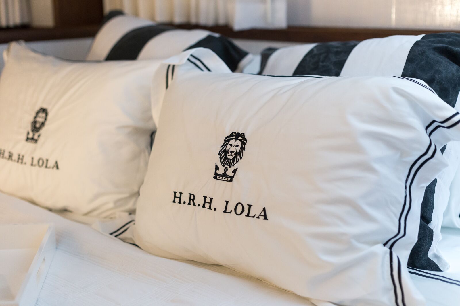 Two pillows on a bed that say h.r.h. lola