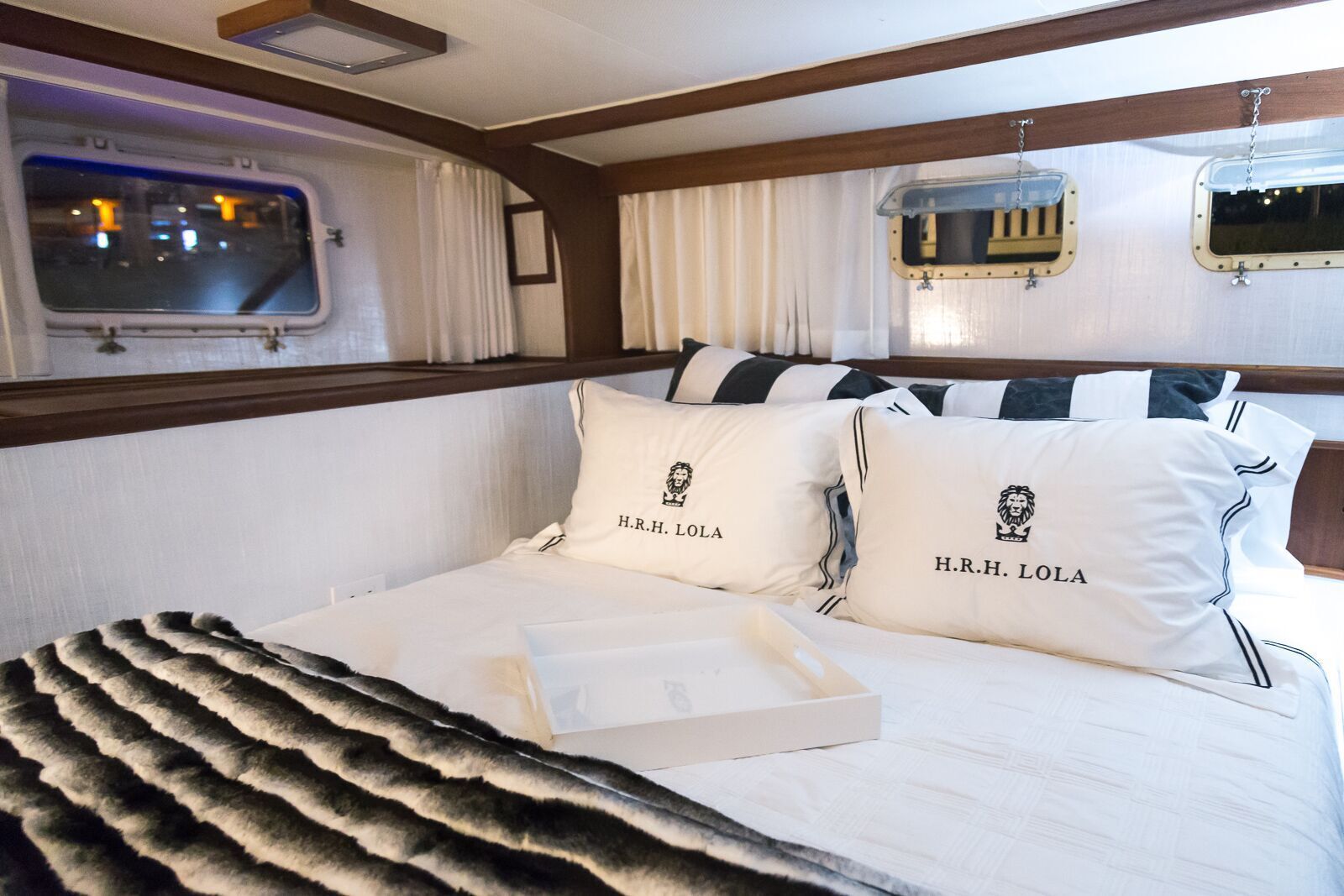 A bedroom on a boat with a bed , pillows and a window.