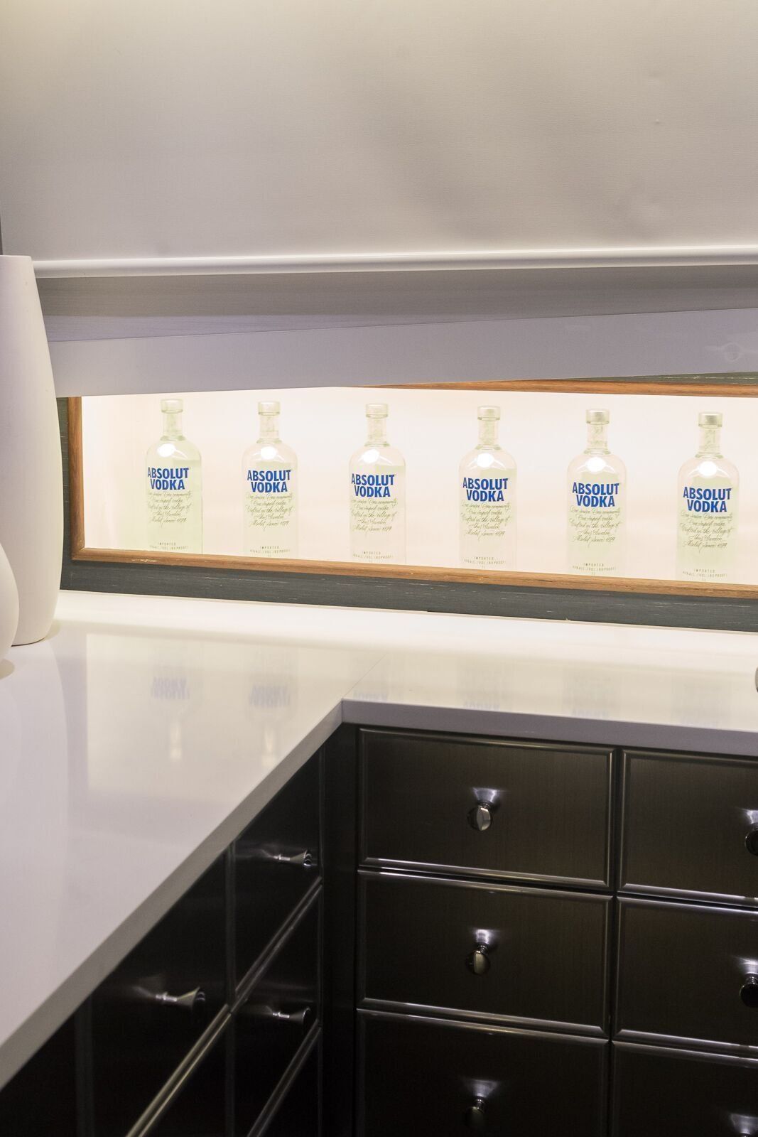A kitchen with black cabinets and a window with bottles of vodka on it