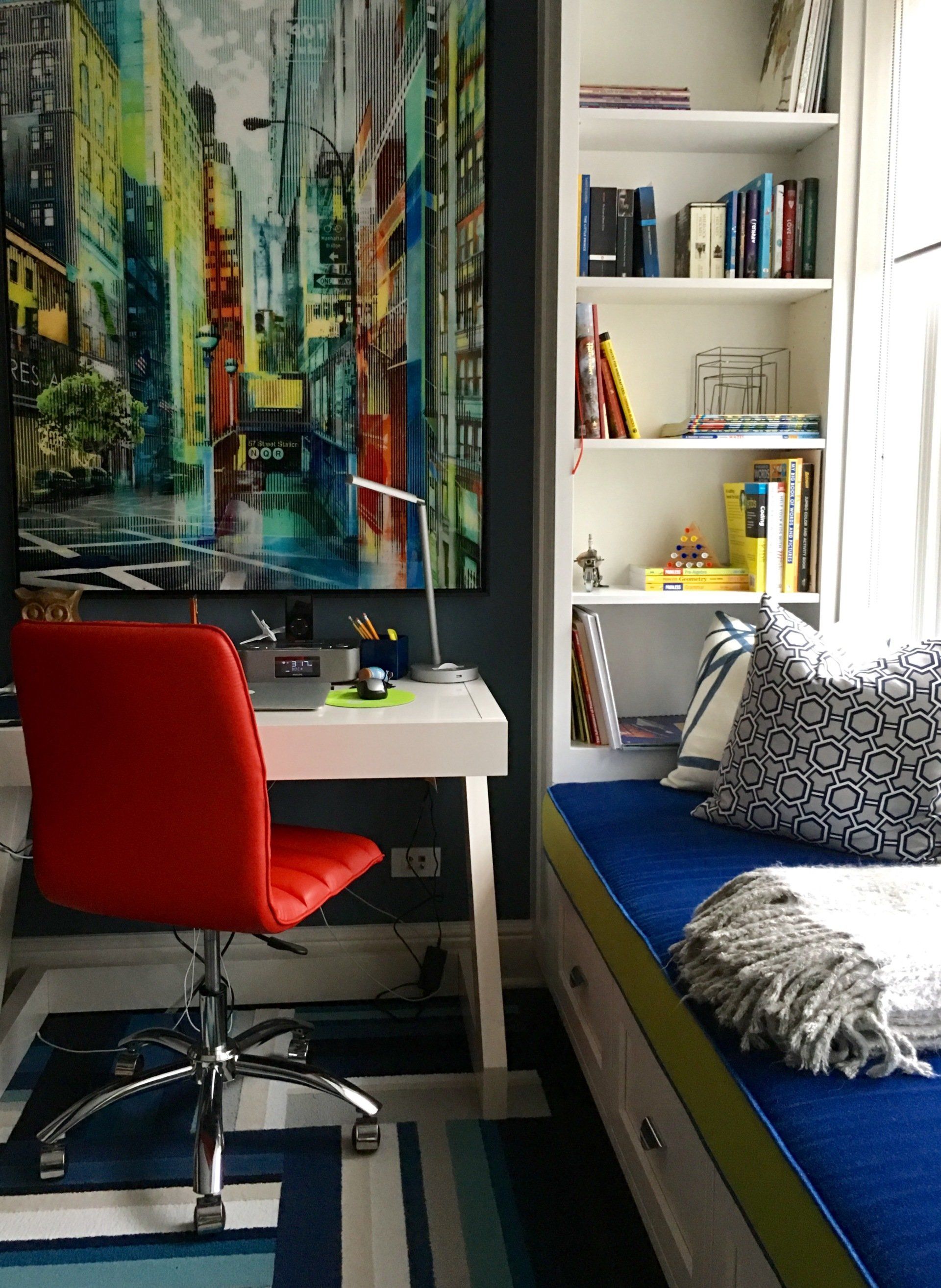 A room with a painting on the wall and a desk with a red chair