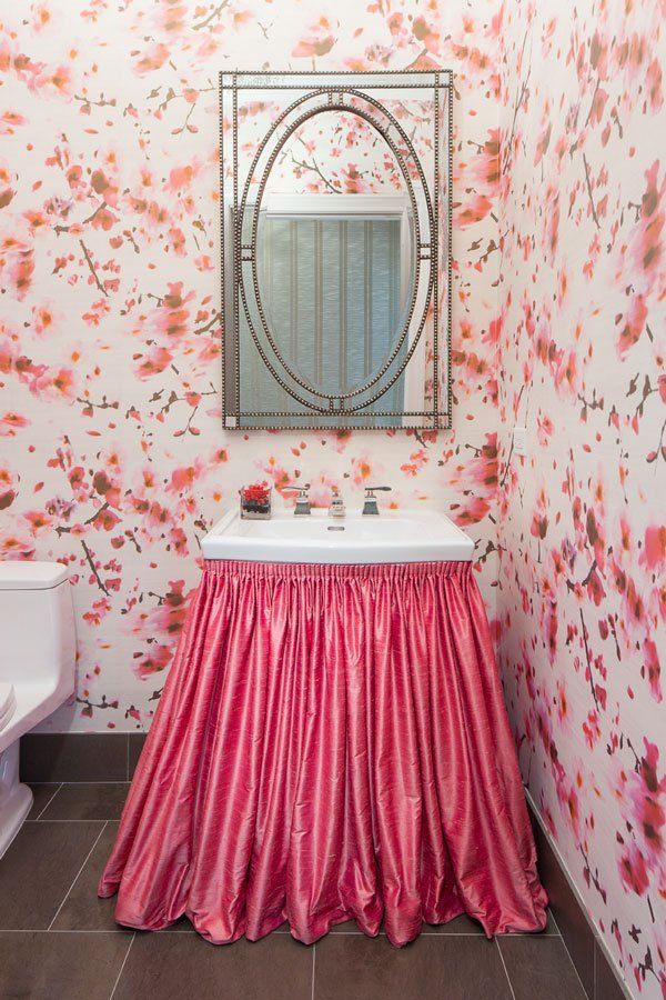 A bathroom with a sink covered in a pink skirt and a mirror.