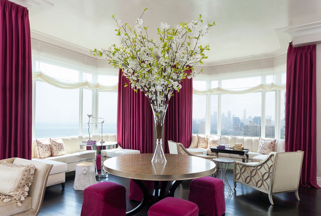 A living room with purple curtains and a vase of flowers on the table.