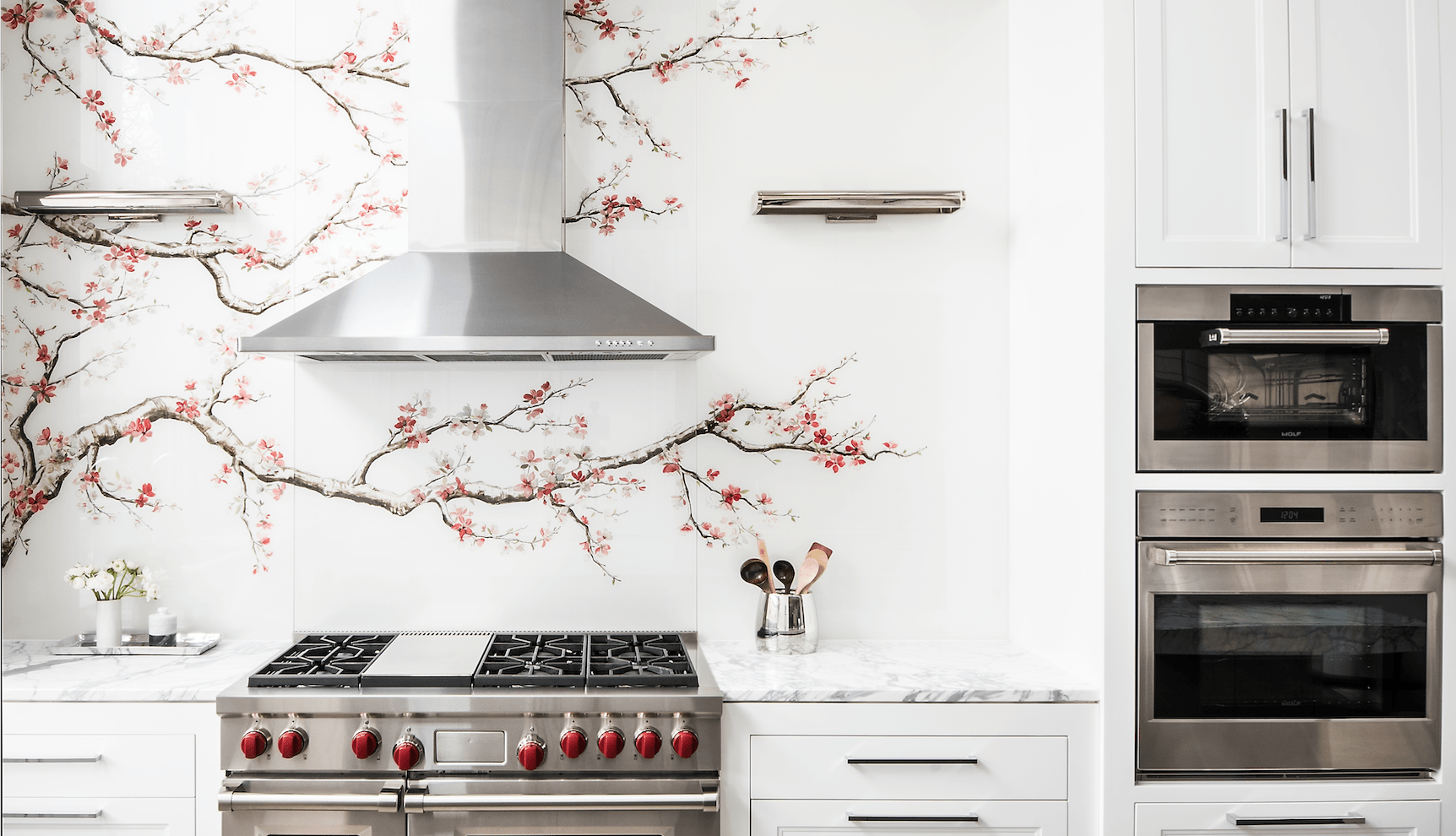 A kitchen with a stove , ovens , and a cherry blossom wall mural.