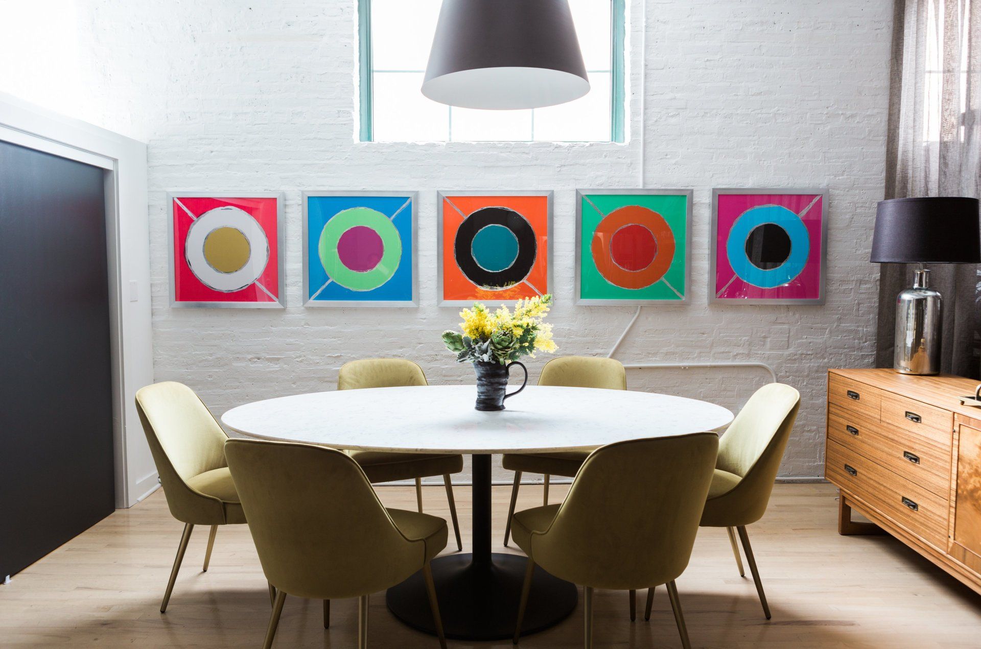 A dining room with a round table and chairs and paintings on the wall